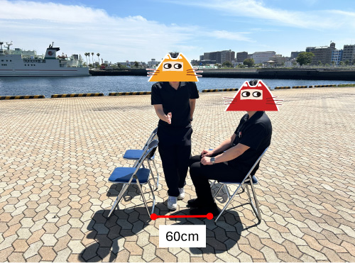 パイプ椅子の前後間隔は60cm。男性Aが着席、男性Bがその前を横切る様子