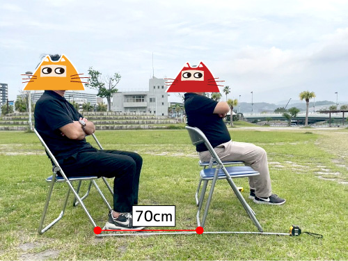 パイプ椅子2脚に着席する男性二人を横から見た図。パイプ椅子の前後間隔は70cm