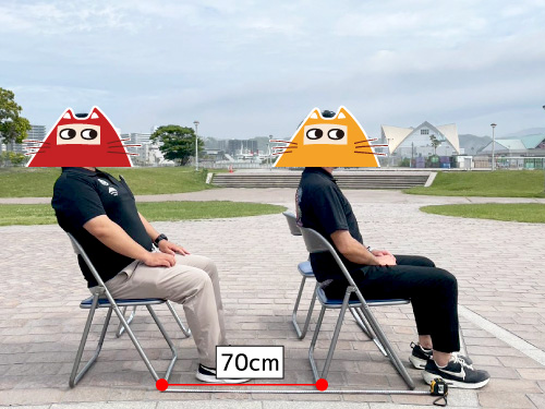 パイプ椅子2脚に着席する男性二人を横から見た図。パイプ椅子の前後間隔は70cm